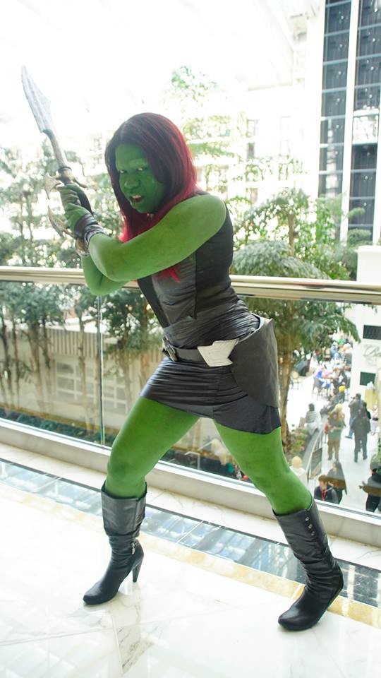 Jay Justice dressed as Gamora from Guardians of the Galaxy in a skirted version, swinging a huge sword as if to attack the viewer